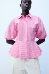 Camisa de popelín a rayas rosadas y blancas, con cuello solapa, mangas abullonadas por debajo del codo con terminación elástica, cintura entallada y bajo en evasé. Cierre frontal con botones ocultos.