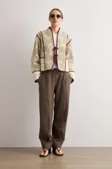 Chaqueta capitoneada de diseño acolchado con estampado paisley en tonos beige y verde, con ribetes y lazos de cierre frontales en color bordó.