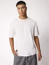 Remera blanca de manga corta y cuello redondo con calce holgado, con una pequeña etiqueta oscura en el borde inferior derecho.