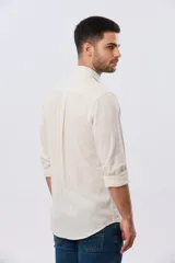 Camisa de lino a rayas finas en tonos beige y blanco, de manga larga con puños vueltos, cuello camisero y cierre frontal de botones. Cuenta con un pequeño logo bordado en el pecho.