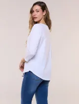 Remera blanca de algodón con elastano, de corte semi holgado, escote bote con ojalillos metálicos frontales, mangas tres cuartos raglán y ruedo asimétrico curvado.