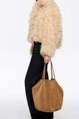 Bolso shopper grande de Bimba y Lola, confeccionado en serraje de piel vacuna con acabado de ante color marrón. Presenta doble asa de hombro y detalle de logo metálico de la marca en la parte inferior.
