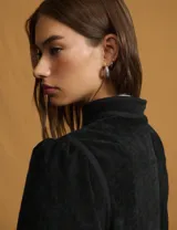 Chaqueta negra de estilo oriental con cuello alto estructurado y cierre frontal mediante nudos decorativos tradicionales. Presenta mangas largas con leve volumen en los hombros y un corte recto.