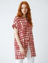 Camisa maternal de corte holgado y largo midi, confeccionada en viscosa suave con estampado geométrico de cuadros en color verde agua y blanco. Presenta cuello camisero, mangas cortas y bolsillos laterales.