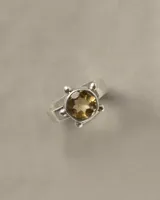 Anillo de plata 925 de banda chata con piedra central de citrino tallada en brillante de 8 mm, engarzada con detalles de esferas metálicas en los extremos.