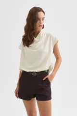 Blusa de poliéster color marfil, de corte holgado, sin mangas y con cuello buche drapeado.