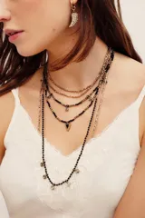 Collar largo múltiple de cuentas doradas y negras con dije triangular central y pequeños dijes colgantes de metal plateado.