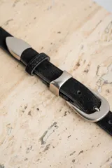 Cinto de cuero negro con textura de gamuza, presenta una hebilla metálica plateada de diseño clásico y puntera metálica a juego.