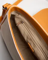 Bandolera combinada de tela texturizada en tono rosado o nude y detalles en símil cuero color tostado. Cuenta con solapa frontal, herrajes metálicos plateados con logo de la marca grabado y correa ajustable.