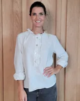 Blusa de manga larga con estampado de rayas verticales finas en tono beige. Presenta cuello redondo con volados, cierre frontal parcial con botones y puños con volados.