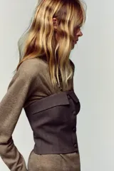 Top bustier corsetero color gris oscuro, con escote recto, solapa y hombros descubiertos. Presenta falsos botones forrados a tono en el frente y cierre lateral con cremallera oculta.