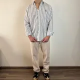 Camisa de manga larga a rayas verticales grises y blancas, con cuello clásico y cierre frontal con botones.