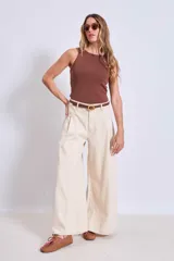 Pantalón de jean color crudo, de corte palazzo y tiro alto, con bolsillos laterales y traseros. Se ajusta a la cintura con cinturón de cuero marrón con hebilla dorada.