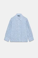 Camisa de cuello solapa y manga larga con puños abotonados. Presenta un diseño de rayas verticales azules y blancas con un estampado floral lineal superpuesto. Cierre frontal con botones.