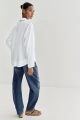 Blusa blanca confeccionada en lino, con cuello polo, escote en V y mangas largas amplias. Presenta un diseño holgado y bajo asimétrico.