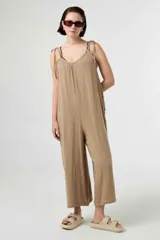 Mono largo de muselina de algodón color beige, con escote en V, tirantes ajustables mediante lazos para atar en los hombros y diseño amplio de corte holgado.