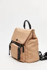 Mochila urbana de nylon color beige, con solapa superior, bolsillo frontal con cierre y correas decorativas con hebillas metálicas. Incluye manija superior y correas ajustables.