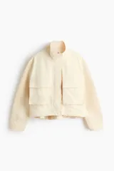 Campera corta de sarga con cuello elevado, solapa rompevientos con cierre y botones a presión ocultos. Diseño oversized con hombros caídos, bolsillos delanteros de fuelle con solapa y cordón elástico ajustable en el bajo.
