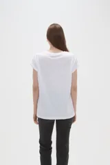 Remera de algodón blanca con estampado frontal de mariposa y texto decorativo en tonos pasteles, de manga corta con dobladillo y calce holgado.