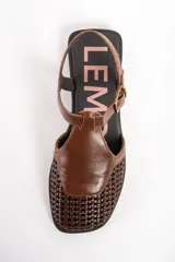 Sandalias de cuero marrón, con puntera cerrada de diseño trenzado, empeine liso y tira ajustable con hebilla en el talón. Cuenta con suela plana y baja.