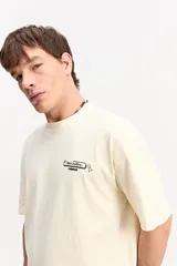 Remera boxy de color beige, de manga corta y cuello redondo, con estampa en la espalda inspirada en código de programación y estética digital.