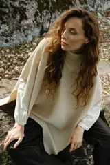 Poncho de tejido de punto color beige, con cuello alto y diseño holgado sin mangas. Presenta una textura acanalada y una caída fluida.