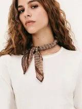 Blusa de manga corta color blanco con cuello redondo y pañuelo estampado con diseño de rombos en tonos marrones atado al cuello.