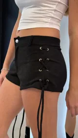 Short negro de gamuza con diseño de cordones cruzados en los laterales y ojales metálicos plateados. Presenta un corte ajustado y tiro bajo.