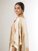 Vestido maxi túnica de corte oversized, color beige y blanco con estampa de hojas de palmera en tonos camel, mangas murciélago y bolsillos laterales.