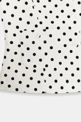 Top de popelín blanco con estampado de lunares negros, de manga corta, cuello redondo y cierre frontal con botones. Cuenta con bolsillos de parche en la parte delantera.