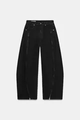 Jeans de corte baggy y tiro medio en color negro. Presenta diseño de cinco bolsillos y detalle de cremalleras verticales en el frente de las piernas con efecto torcido.