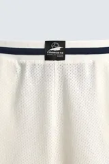 Short deportivo de tejido de punto con estructura abierta, color blanco con vivos a contraste en azul marino. Presenta cintura elástica, bolsillos frontales, aberturas laterales en el bajo y etiquetas conmemorativas de la Copa Mundial de la FIFA Francia 98.