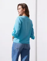 Blusa de gasa con estampado geométrico en tonos negro, gris y celeste. Tiene cuello redondo y mangas 3/4 amplias con abertura y botón.