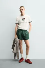 Camiseta de corte relajado confeccionada en piqué de algodón color crudo. Presenta cuello redondo, mangas cortas con ribetes a contraste y estampado frontal con el logo de Italia 90 FIFA World Cup.