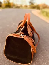 Bolso de viaje grande de cuero vacuno color negro con detalles en marrón. Tiene herrajes metálicos, gran superficie interna, asa de mano y correa para el hombro.