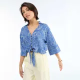 Camisa azul con estampado floral en blanco, de corte oversize, mangas tres cuartos, escote en V con cuello y detalle de nudo en el frente.