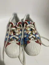 Championes Adidas modelo Superstar, con diseño estampado floral en tonos azules, rojos y amarillos sobre base de tela, con la clásica puntera de goma blanca y cordones blancos.