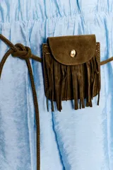 Vestido corto de color celeste con cuello solapa, cierre frontal de botones y manga larga con puños elásticos. Presenta cintura elástica, falda con volantes y un cinturón fino con un pequeño bolsillo de flecos incorporado.