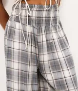 Pantalón de viscosa estilo aladín con estampado a cuadros en tonos grises, blancos y azules. Presenta cintura elástica fruncida y puños ajustados en los tobillos de corte ancho.