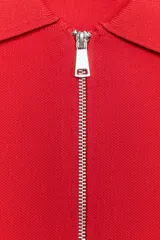 Chaqueta de punto color rojo, con cuello solapa, manga corta y cierre frontal con cremallera. Cuenta con acabados en rib.