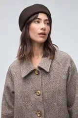 Chaquetón de lana fina sin teñir, con cuello camisero, cierre frontal de botones y bolsillos delanteros. Diseño de corte recto y estructura clásica.