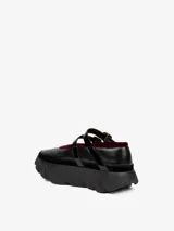 Zapato tipo bailarina de cuero negro con borde de terciopelo rojo, doble tira con hebilla dorada y suela de goma con diseño de neumático.