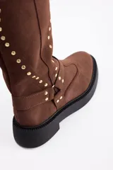 Bota de caña alta confeccionada en cuero vacuno, color negro, con diseño de tachas metálicas dispuestas en forma de arco a lo largo de la caña y correa decorativa con hebilla en la zona del tobillo. Presenta suela track de goma robusta.