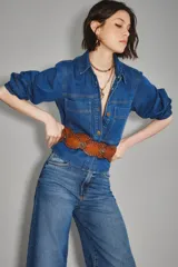 Camisa crop de denim azul, con cuello camisero, botones frontales dorados, dos bolsillos en el pecho y mangas abullonadas.