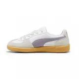 Championes Puma modelo Palermo LTH, con diseño de perfil bajo, cuerpo de cuero blanco, detalles en gamuza gris y franja lateral en color lila. Cuenta con suela de goma color caramelo y logo dorado en el lateral.