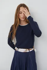 Remera de manga larga en color azul marino, confeccionada en tejido suave. Presenta un delicado detalle de bordado festoneado en color blanco tanto en el cuello redondo como en los puños, aportando un toque distintivo a esta prenda básica.