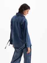 Camisa de denim azul profundo, de calce amplio y relajado, con cuello camisero clásico, hombros caídos y mangas largas con recortes y lazos regulables en los puños.