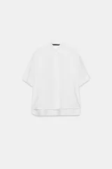 Camisa blanca de manga corta con vuelta en los puños, cuello solapa y bajo asimétrico con aberturas. Cuenta con cierre frontal con botones ocultos por solapa.
