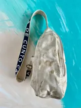 Mochila Kiri de cuero natural de la marca Carolina De Cunto, con diseño artístico pintado a mano de flores multicolores en el frente. Cuenta con una correa bandolera negra con el nombre de la marca en letras blancas y cierre superior con cremallera.