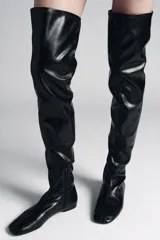 Bota mosquetera de caña extra larga, color negro, con diseño ajustado y suela plana. Presenta punta redonda y cierre lateral.